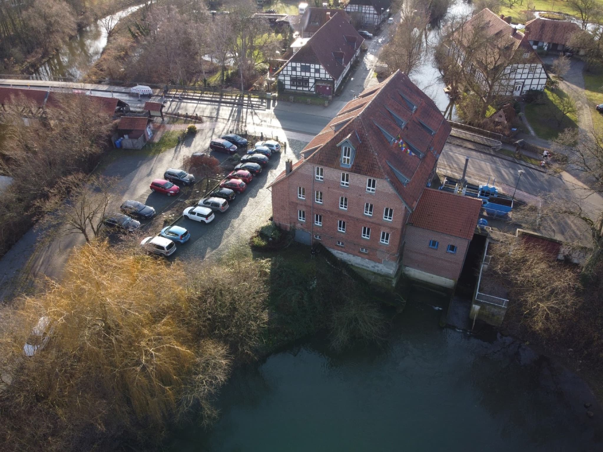 Luftaufnahme der Okermühle: das Gebäude steht direkt am Wasser der Oker, umgeben von Fachwerkhäusern und dem hauseigenen Parkplatz